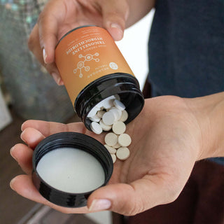 Hand holding open Trigonelline Hydrochloride bottle with white tablets.