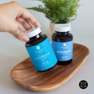 Hand holding L-Ergothioneine and Spermidine supplements on a wooden plate with greenery in the background.