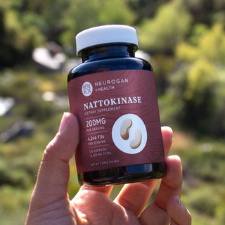 Hand holding Nattokinase 200mg supplement bottle with 120 capsules in natural light.
