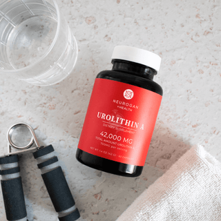 Neurogan Urolithin A dietary supplement bottle on a counter with fitness equipment and a glass of water.