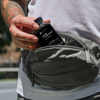 A person holding a bottle of immune support tablets while wearing a waist bag, outdoors.