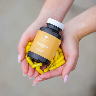 Hands holding a bottle of Berberine with yellow capsules, showcasing a supplement for health and wellness.