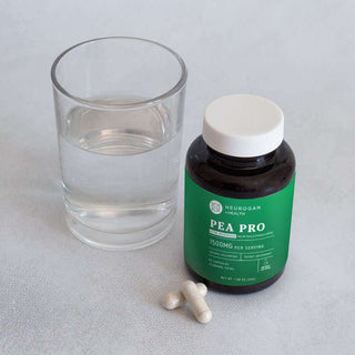 Neurogan Pea Pro supplement bottle with capsules and a glass of water on a light surface.