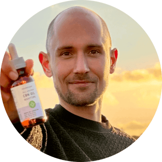 Man holding CBN oil bottle against a sunset backdrop, showcasing hemp-derived wellness products.