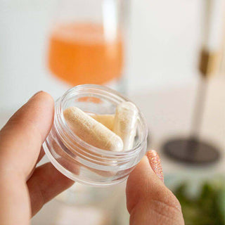 Person holding a clear jar with dietary capsules, with a blurred drink in the background.
