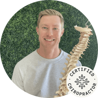 Certified chiropractor holding a model spine, smiling in a natural setting.