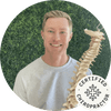 Certified chiropractor holding a model spine, smiling in a natural setting.