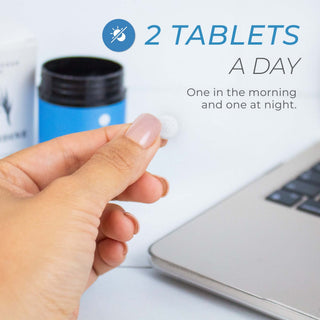 Person holding a Spermidine tablet with dosage instructions beside a laptop.
