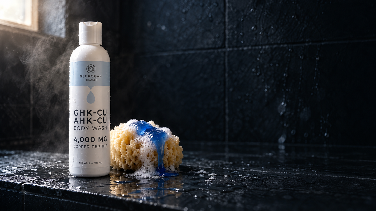 GHK-Cu + AHK-Cu Body Wash bottle on a wet slate shower ledge beside a sea sponge and a ribbon of blue gel