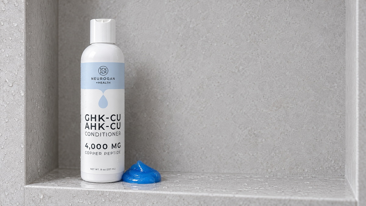 GHK-Cu + AHK-Cu Hair Conditioner bottle on a pale stone bath ledge beside a curl of blue conditioner