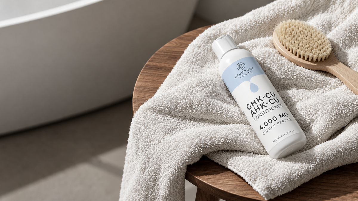 GHK-Cu + AHK-Cu Hair Conditioner bottle on a stone ledge beside a lock of wet hair coated in blue conditioner