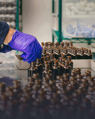 Worker in purple gloves arranging dark glass bottles in a laboratory setting for production and quality control.