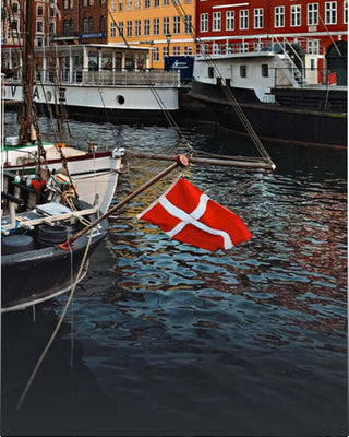 Danish flag waving from a boat in a colorful harbor, reflecting on calm water.
