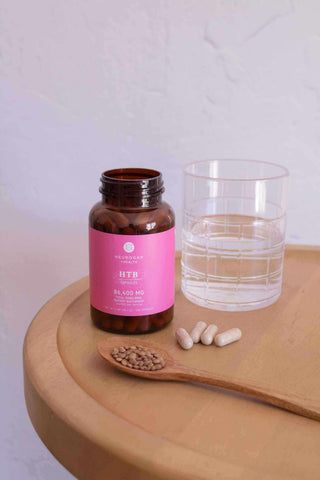Brown supplement bottle with pink label, glass of water, and capsules on a wooden table.