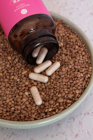 Vegan supplement capsules spilling from a brown bottle onto a bed of lentils in a green bowl.