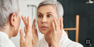 Mature woman applying skincare cream while looking in the mirror, highlighting a self-care routine for healthy aging.