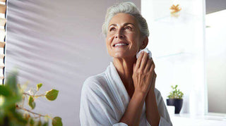 Mature woman in a bath robe with radiant skin using skincare in natural light