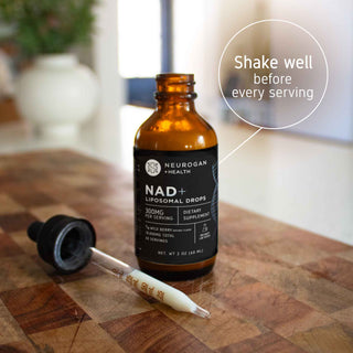 NAD+ Liposomal Drops bottle with dropper, on wooden surface, shake well before each serving instruction.