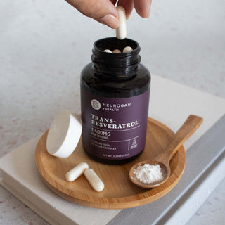 Trans-Resveratrol bottle with capsules and powder on wooden tray, hand holding one capsule.