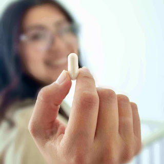 Smiling woman holding a white capsule supplement.