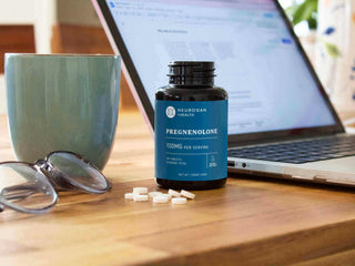 Bottle of Pregnenolone supplement on desk next to a mug and glasses, illustrating health and wellness.