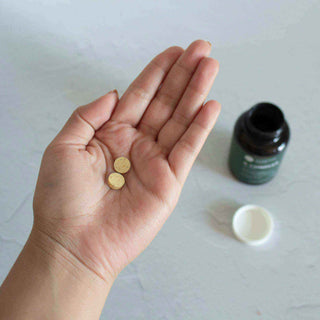 Hand holding two round yellow pills with a bottle in the background, representing vitamins or supplements.