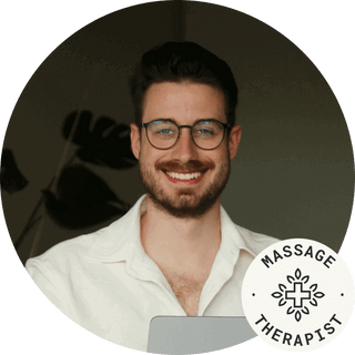 Smiling male massage therapist with glasses, promoting relaxation and wellness.