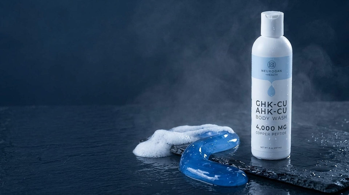 GHK-Cu + AHK-Cu Body Wash bottle on dark slate behind a ribbon of blue gel turning into lather