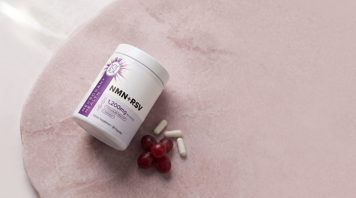 NMN + Resveratrol jar on pale pink stone with capsules and red grapes