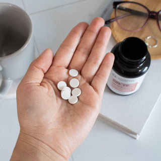 GHK-CU Tablets - White tablets in an open hand, with a black-labeled bottle on a table nearby.